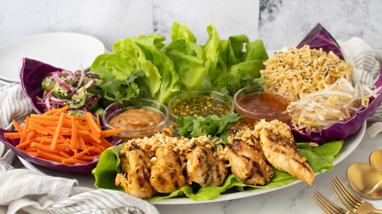 Thai lettuce wrap platter with various vegetables, chicken, noodles, and sauces