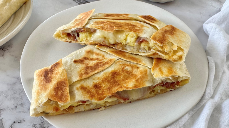 Copycat Crunchwrap holding eggs and bacon in flour tortillas split in half on plate