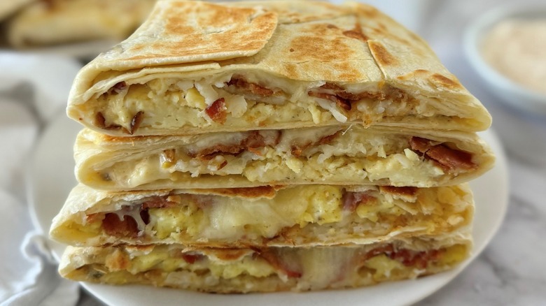 Closeup of cut copycat Crunchwraps holding eggs and bacon in flour tortillas stacked on a plate