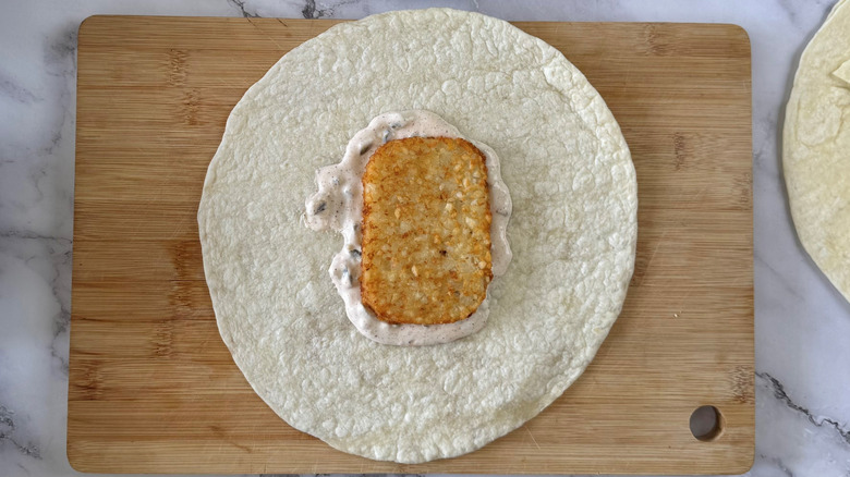 flour tortilla with a hash brown patty on a cutting board