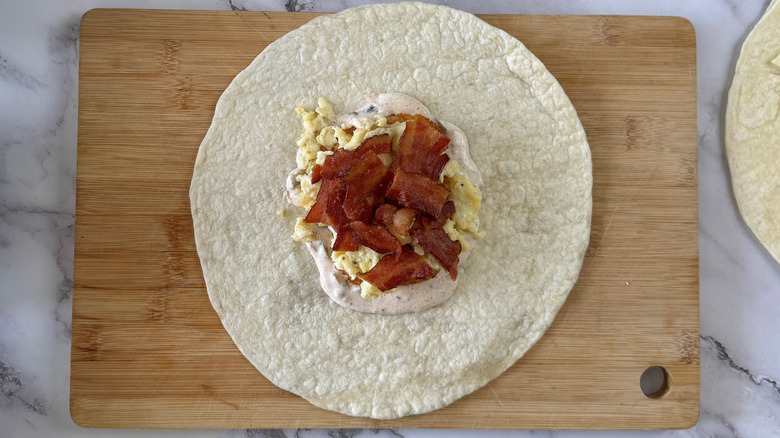 flour tortilla with scrambled eggs and bacon on a cutting board