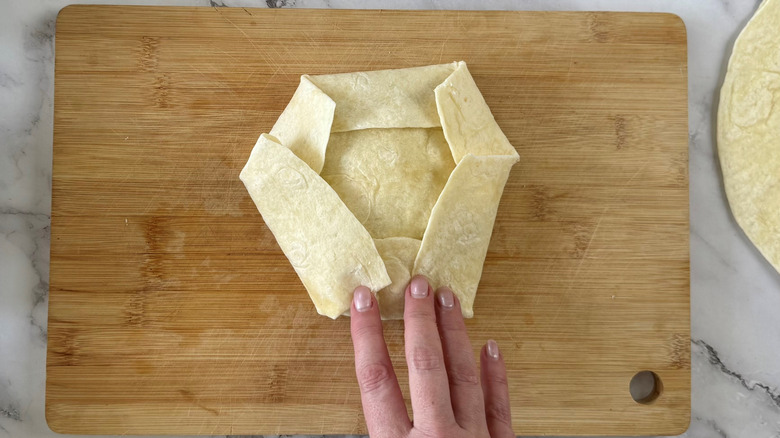 hand touching folded flour tortilla sitting on top of cutting board