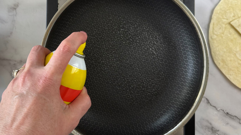 hand squirting cooking spray on frying pan