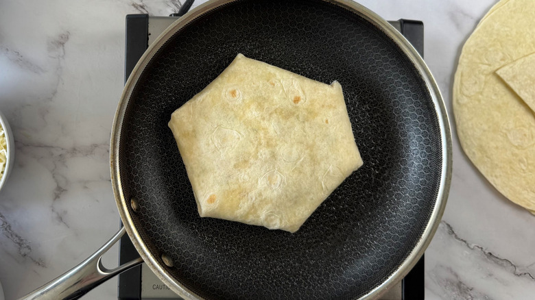 folded flour tortilla in frying pan with extra tortillas on a marble surface