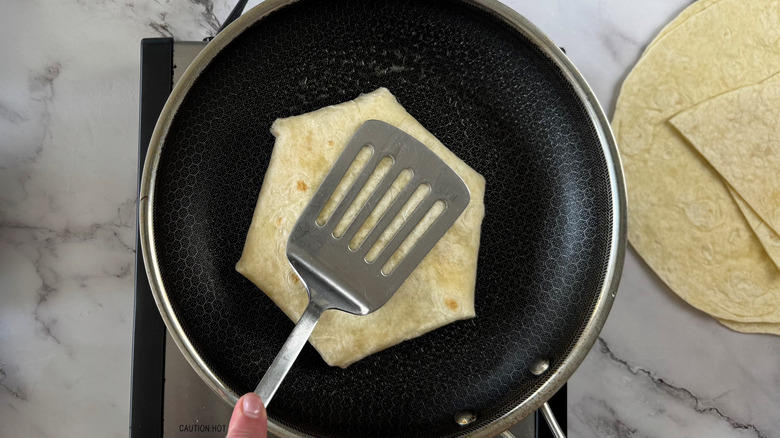 aerial view of hand pressing spatula on folded flour tortilla in frying pan