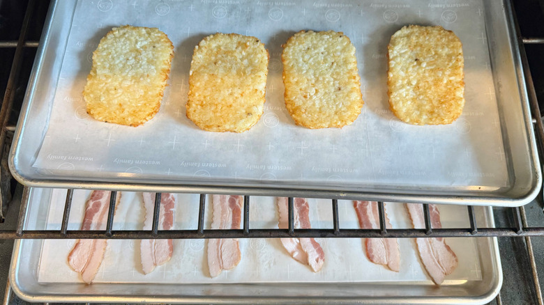 frozen hash browns and bacon on two lined baking sheets in the oven