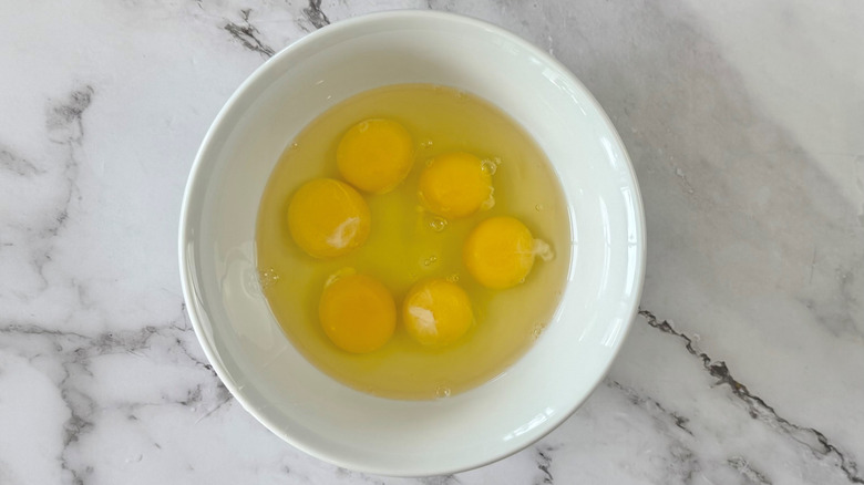 raw eggs in a white bowl on a marble surface