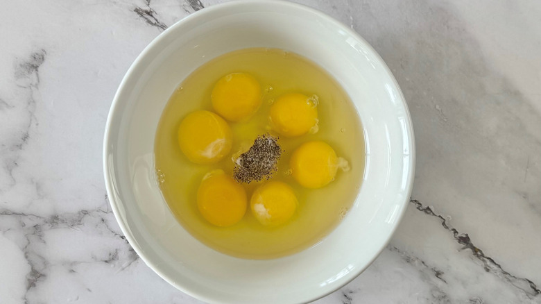 raw eggs and pepper in a white bowl on a marble surface