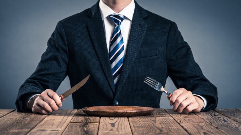 man in suit holding fork and knife over empty plate