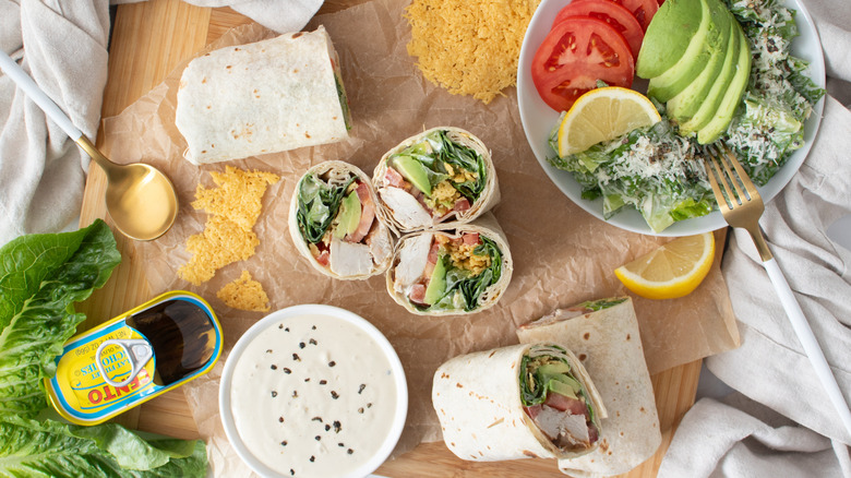 half wrap sandwiches on a countertop with vegetables, cheese, and an opened can of anchovies