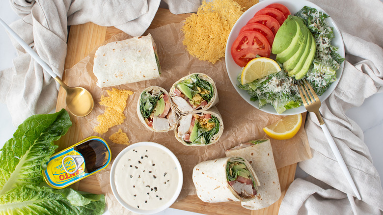 half wrap sandwiches on a countertop with vegetables, cheese, and an opened can of anchovies
