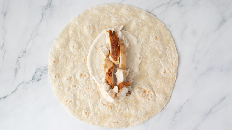 one flour tortilla with cooked chicken and salad dressing