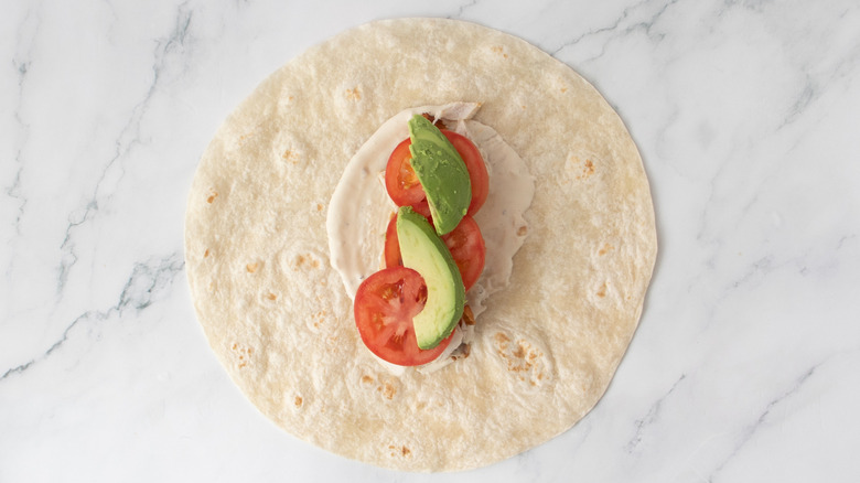 one flour tortilla with cooked chicken, vegetables, and salad dressing