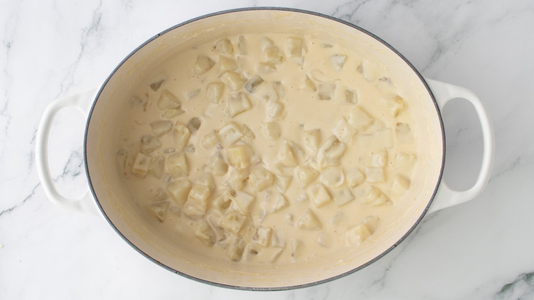 chopped potatoes in orangish liquid in a white pan