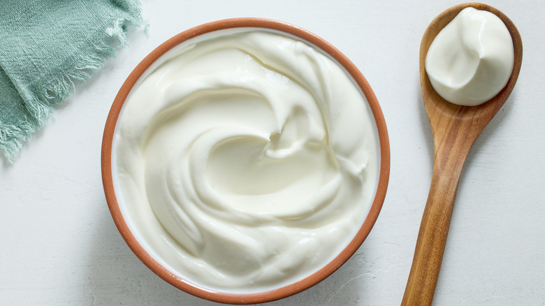 Sour cream in a bowl with a filled wooden spoon on the side