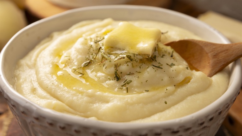 Bowl of mashed potatoes topped with dried herbs and a pat of butter
