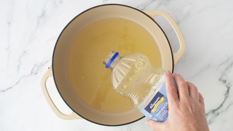 hand pouring oil into a white pot