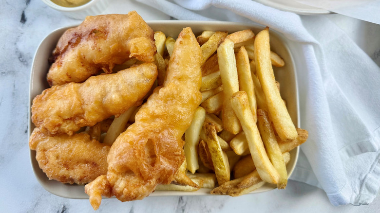 battered chicken strips on a rectangular white plate with french fries sitting next to a crumpled white napkin