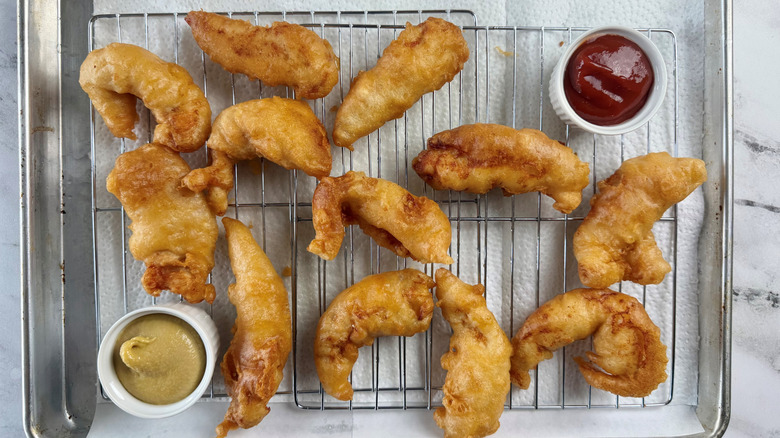 12 battered chicken strips on a wire rack with small bowls of ketchup and mustard