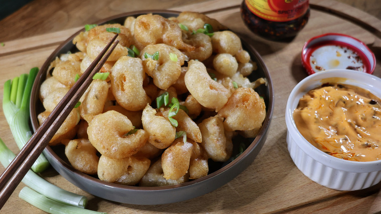 plate of tempura-fried popcorn shrimp with chopsticks resting on it next to ramekin of orange chili crisp dipping sauce