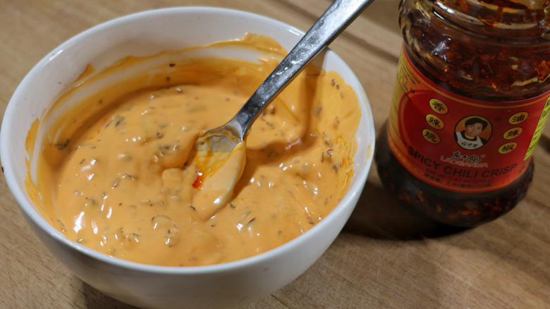 bowl of orange sauce with spoon in it next to bottle of chili crisp