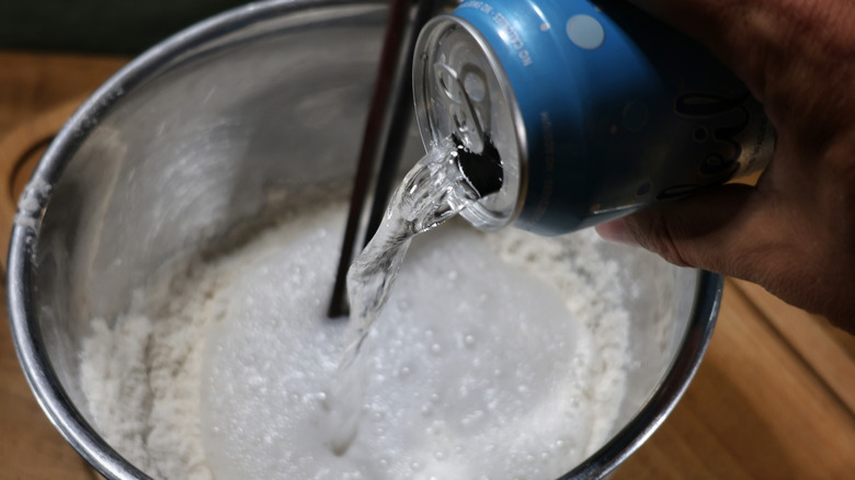 hand pouring seltzer water into mixing bowl of flour
