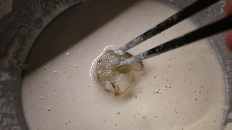 shrimp held by chopsticks being dipped in tempura batter