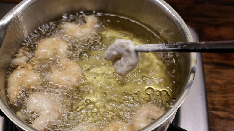 battered shrimp held by chopsticks being dropped into pot of frying shrimp