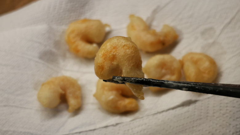 chopsticks holding tempura-style fried shrimp above paper towel-lined plate of fried shrimp