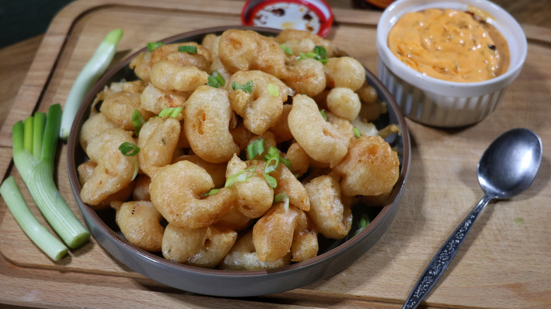 plate of tempura fried popcorn shrimp on cutting board with dipping sauce and scallions