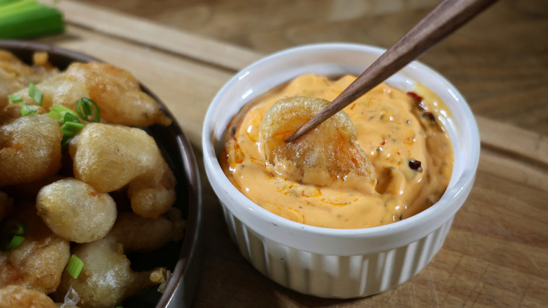 chopsticks dip tempura fried popcorn shrimp into ramekin of orange dipping sauce