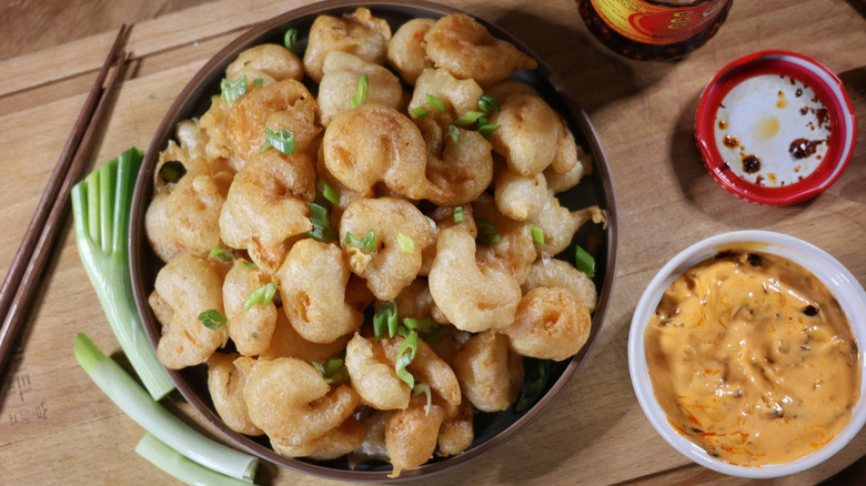 overhead shot of plate of tempura-style popcorn shrimp on cutting board with scallions and chili crisp diping sauce