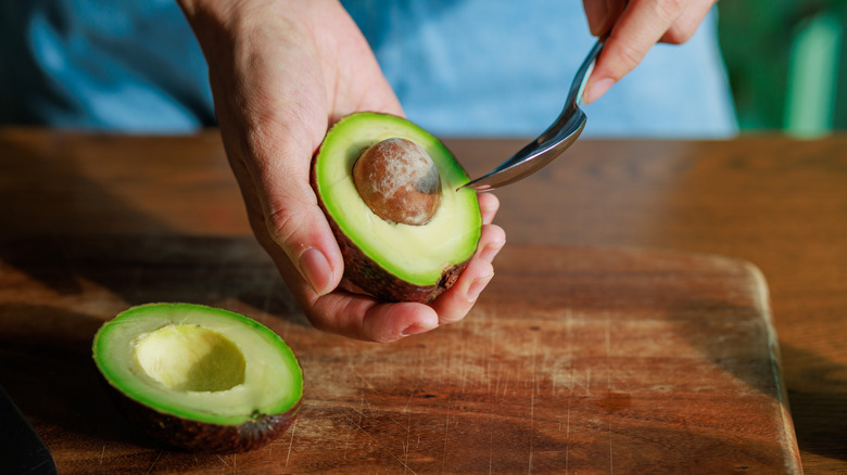 Scooping the seed out of a halved avocado