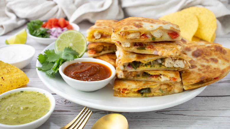 sliced chicken quesadillas stacked on a white plate surrounded by dips