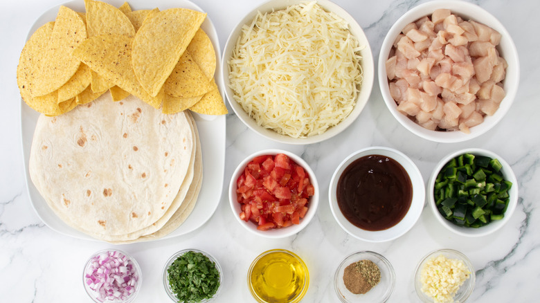 raw chicken, shredded cheese, tortillas, diced vegetables, and seasonings laid out on marble surface