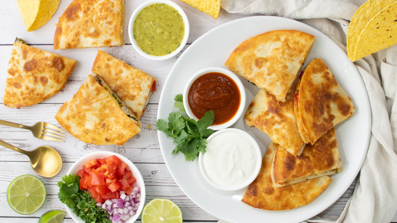 chicken quesadillas on a white plate surrounded by dips and diced vegetables
