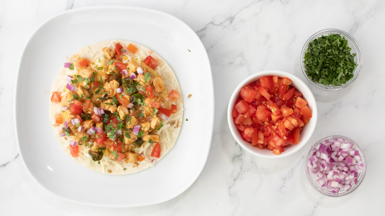 flour tortilla topped with chicken and vegetables next to bowls of diced vegetables