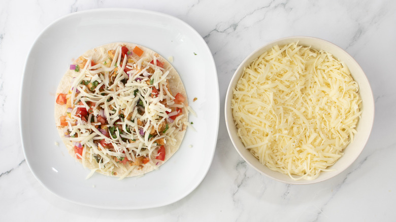 flour tortilla topped with chicken, vegetables, and cheese on a white plate