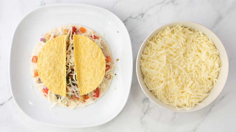 flour tortilla topped with a split taco shell next to a bowl of cheese