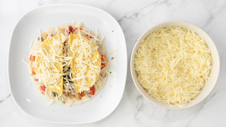 flour tortilla topped with shredded cheese on plate next to bowl of cheese