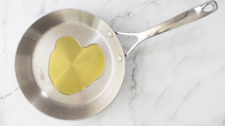 a pool of oil in silver-colored frying pan on marble surface