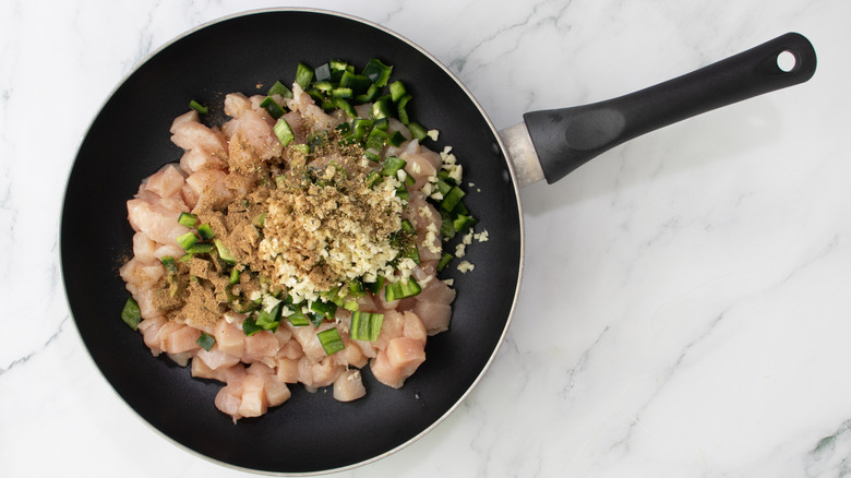 raw chicken and spices in a black frying pan
