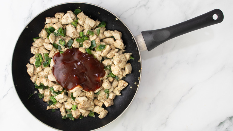 cooked chicken, peppers, and barbecue sauce in a black frying pan