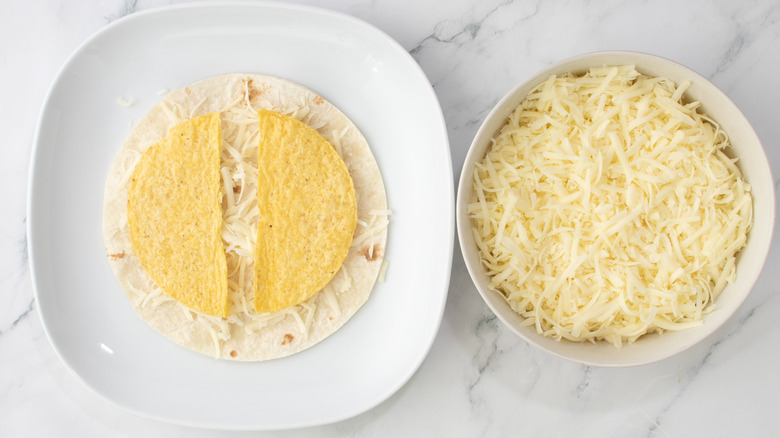 flour tortilla topped with shredded cheese and a split taco shell