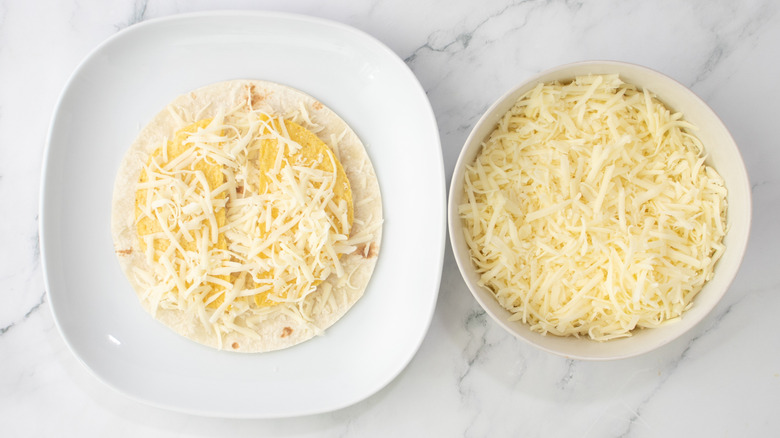 flour tortilla topped with shredded cheese next to bowl of cheese