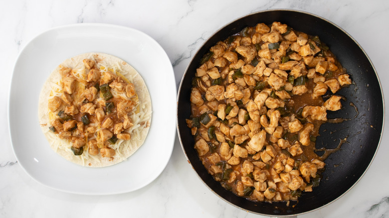 flour tortilla topped with chicken and peppers next to pan of cooked chicken