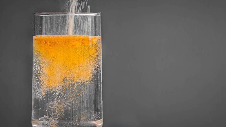 A drink mix being poured into a glass of water