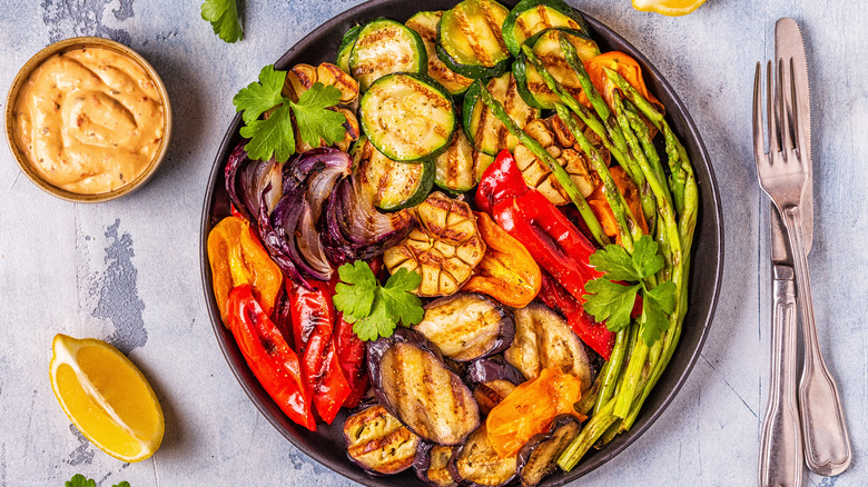 A plate of grilled fruits and vegetables on a rustic background with sauce and a lemon slice