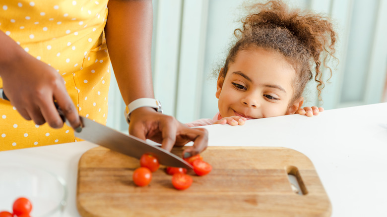   mujer cortando tomate cherry con niño viendo