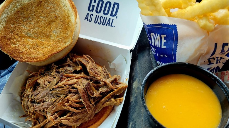 A Culver's pot roast beef sandwich with the top bun open, a side of fries, and cheese sauce